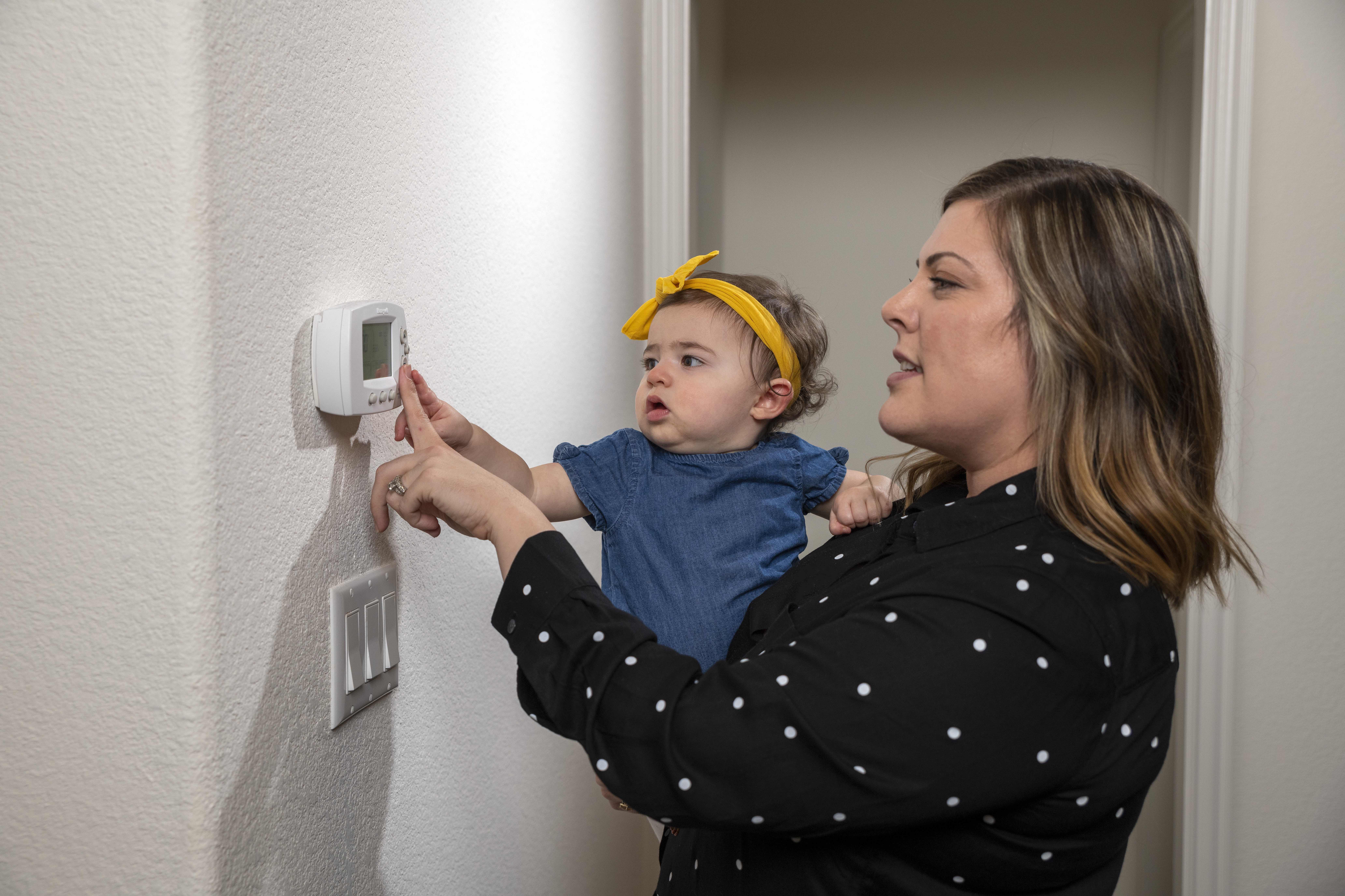 Mom holding a baby and adjusting the thermostat